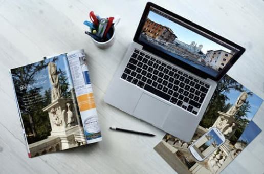 laptop, cell phone, newspaper, photographs and pens on a table